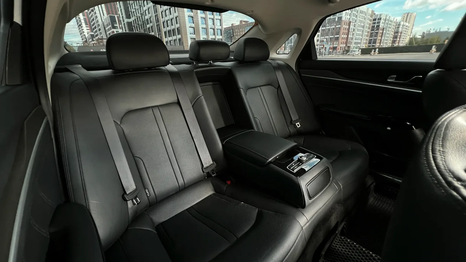 Задний кожаный ряд белой KIA K5 с широким подлокотником, такой седан часто бронируют и берут в аренду с водителем для деловых поездок