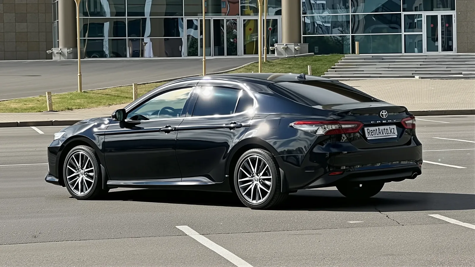 Чёрная Toyota Camry 75 снята сзади на ровной площадке, автомобиль задействуют в обслуживании деловых клиентов с водителем