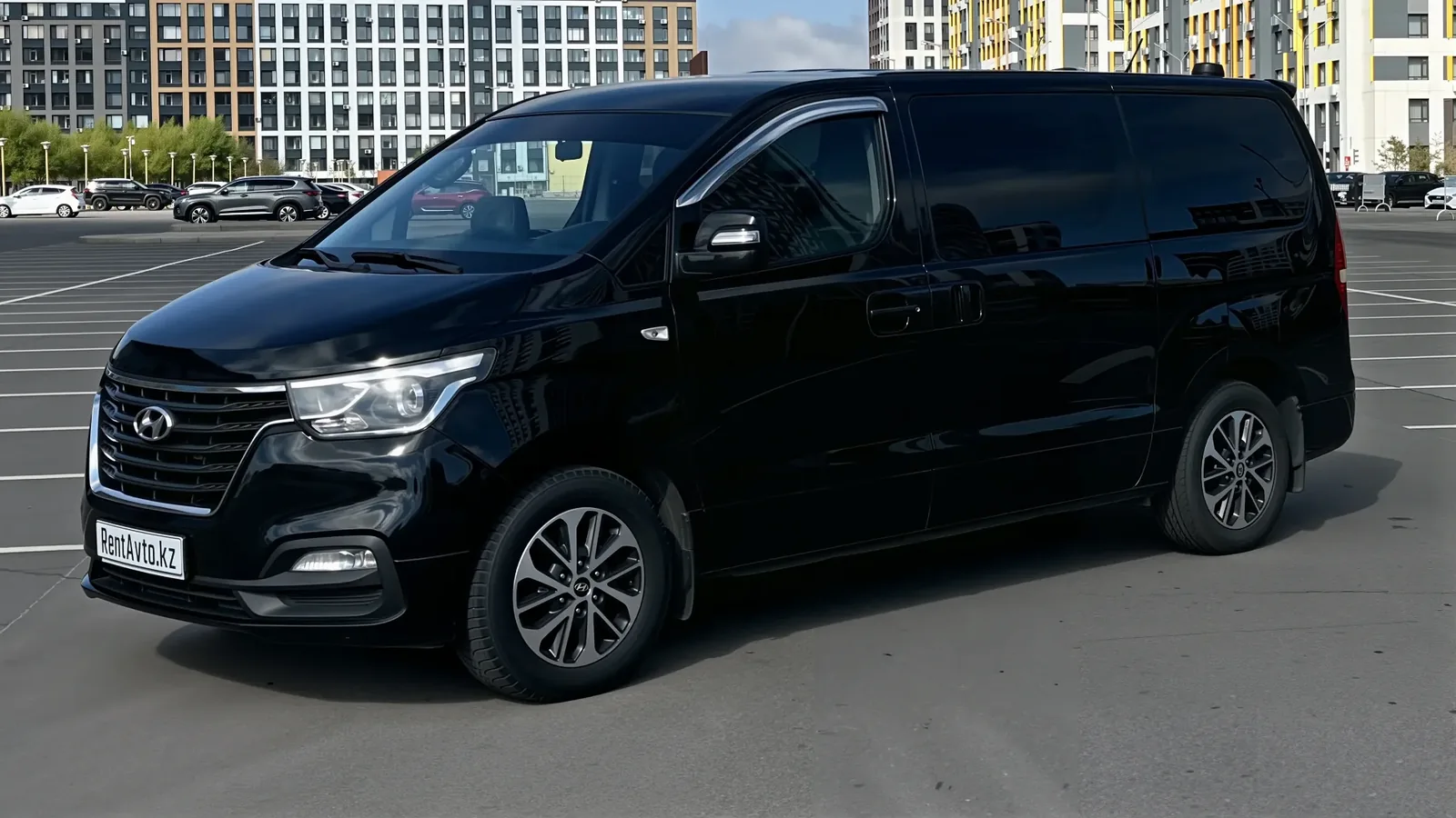 Чёрный минивэн Grand Starex припаркован у обочины, на фоне видна городская застройка и часть проезжей части