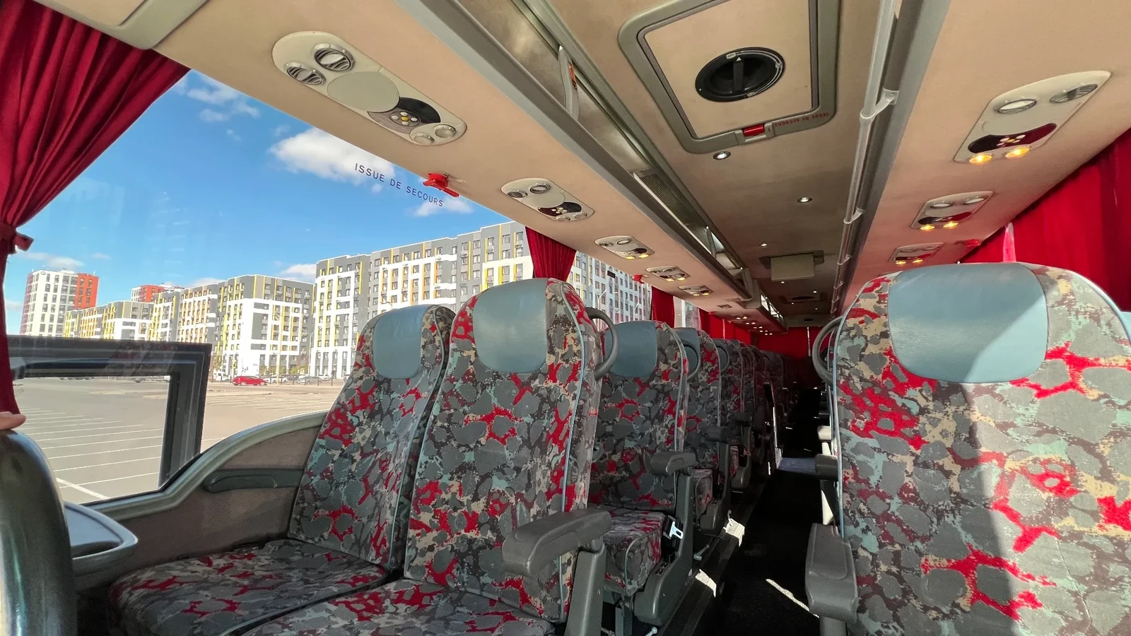 Вид по салону автобуса VanHool с полками для ручной клади и яркими занавесками, используемого для перевозки пассажиров по городу