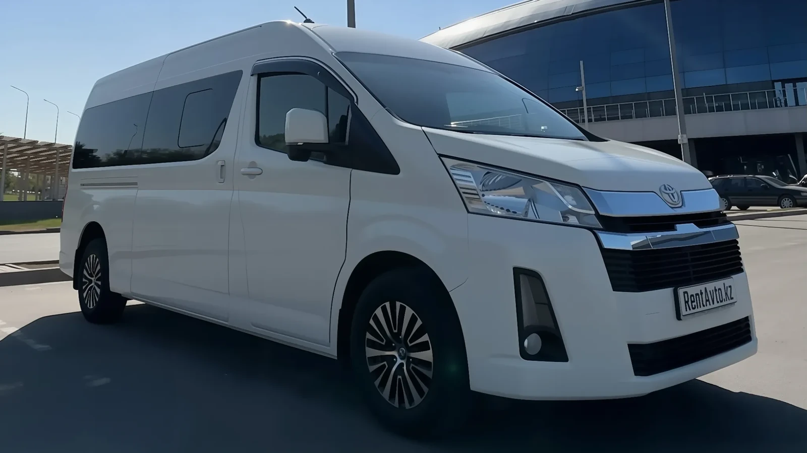 Белый Toyota Hiace на 9 мест, снятый спереди возле городского комплекса