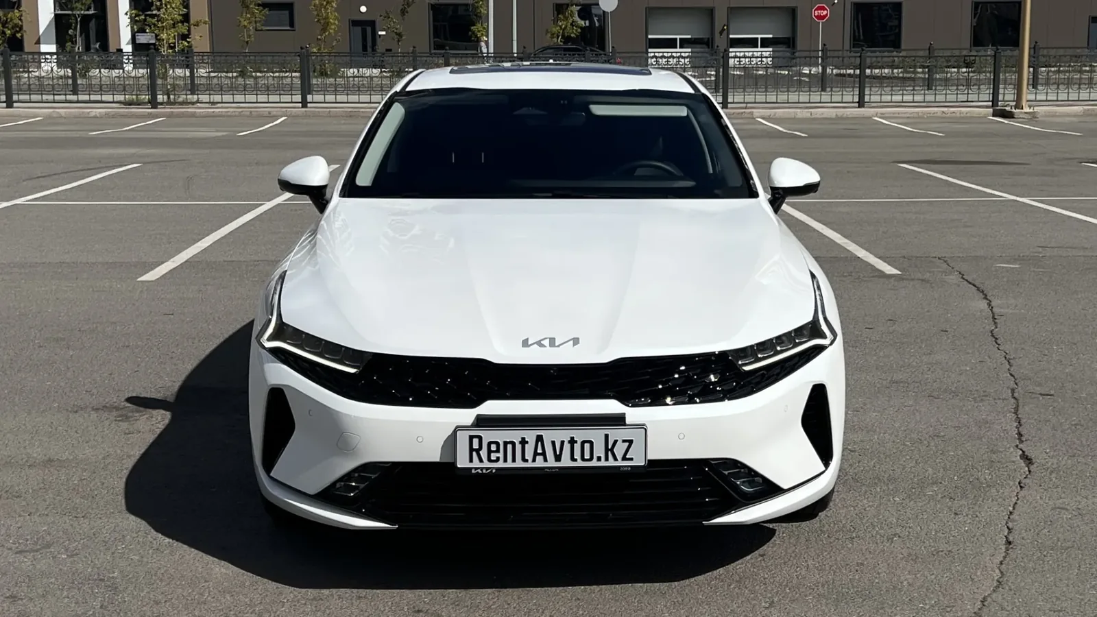 Белая KIA K5 на открытой площадке перед выездом за город с профессиональным водителем из Астаны