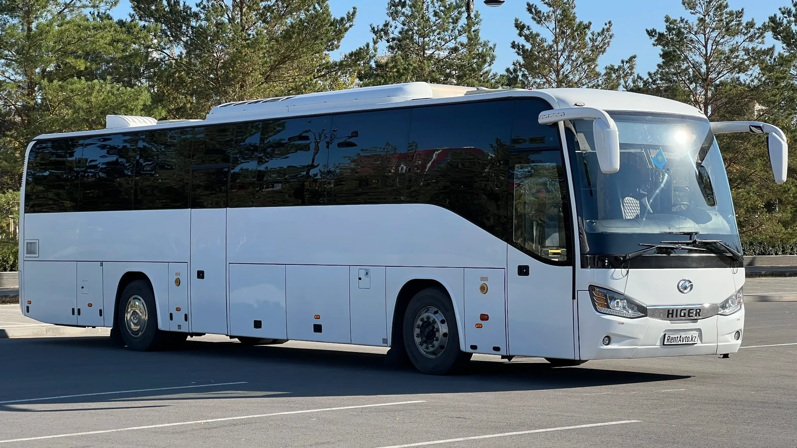 Белый автобус Higer на 54 места снят сбоку на открытой площадке, его используют для обслуживания туристических групп
