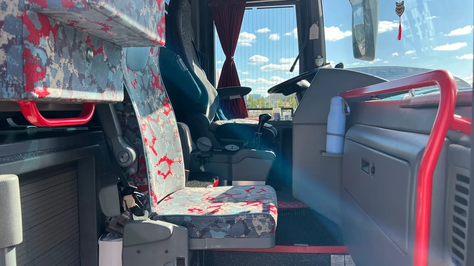 Вид по салону автобуса VanHool с полками для ручной клади и яркими занавесками, используемого для перевозки пассажиров по городу