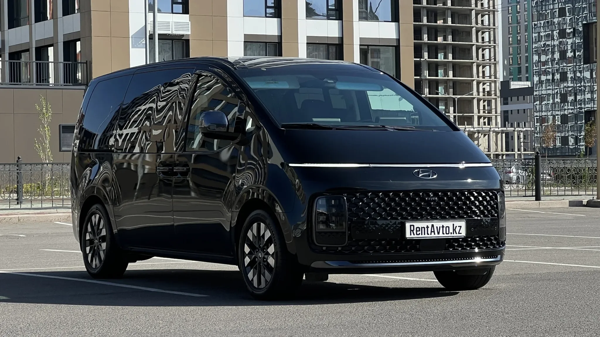 Чёрная Hyundai Staria LUX на 6 мест с фирменной передней оптикой припаркована у современных высотных домов