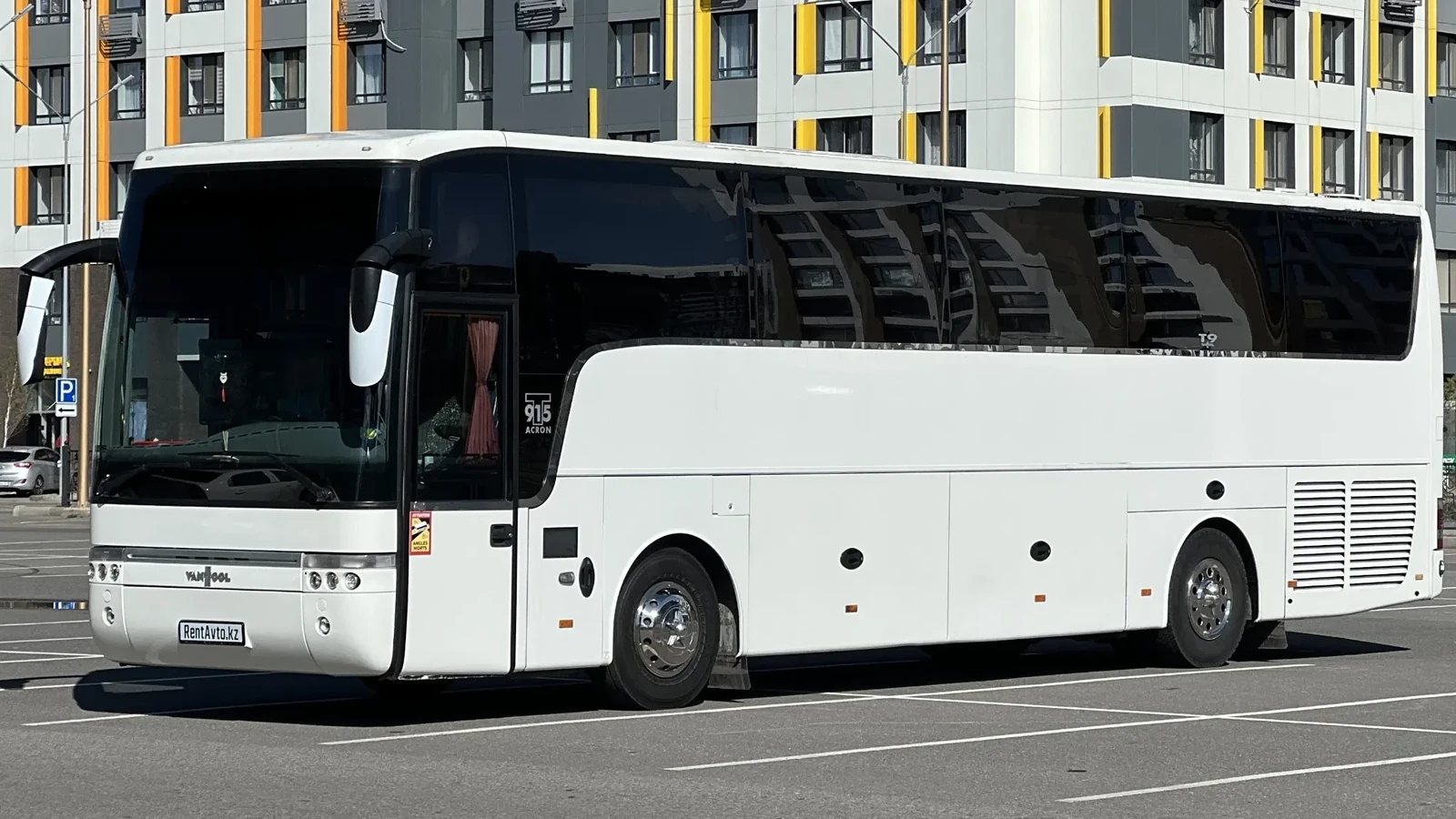 Белый автобус VanHool стоит на городской улице перед выездом на заказ клиентов, заранее запланировавших поездку